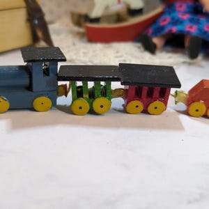 Op de afbeelding: Een speelgoedtreinset met een blauwe locomotief, groene en rode wagons en een rode sluitwagen. De trein heeft gele wielen en zwarte daken.