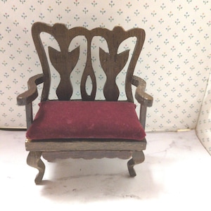 Puede incluir: Una silla de madera en miniatura con respaldo tallado y un cojín de terciopelo burdeos.