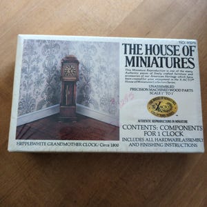 May include: A box for a miniature Hepplewhite grandmother clock, circa 1800. The box features an image of the clock in a room setting. Text on the box reads "The House of Miniatures" and includes assembly instructions.