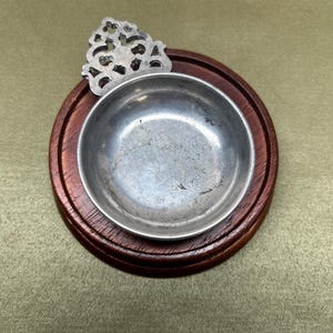 May include: A small, round, antique silver bowl set in a dark brown wooden base. The bowl has a decorative silver filigree accent. The wooden base is approximately 4 inches in diameter.