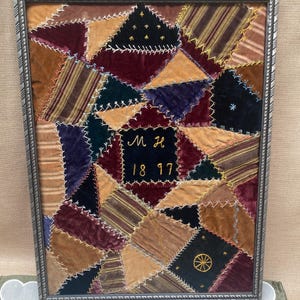Könnte beinhalten: Gerahmte antike Patchwork-Textilkunst. Das Kunstwerk zeigt ein geometrisches Design aus Samtflicken in verschiedenen Farben, darunter Burgunderrot, Gold und Marineblau. Die Flicken sind mit kontrastierendem Faden zusammengenäht. Der mittlere Flicken hat die Initialen "M H" und das Jahr "1817".
