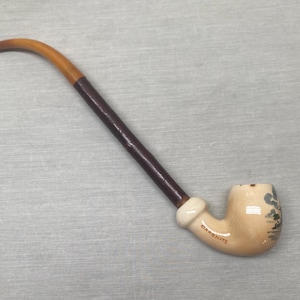 Puede incluir: Una pipa de tabaco vintage con una boquilla curva y un cuenco. El vástago es marrón y beige, que pasa a un cuerpo marrón oscuro. El cuenco beige presenta un diseño de paisaje y la palabra "DAROHITE".