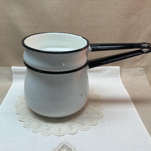 May include: A white enamel double boiler pot with a black rim and two black handles. The pot features a rounded base and a nested upper section, both finished in a smooth white enamel coating with contrasting black trim along the edges.