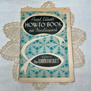 May include: A vintage softcover book titled Aunt Ellen's HOW-TO BOOK on Needlework for readers of THE WORKBASKET. The cover features a teal and white spiderweb-like lace pattern with two black oval text boxes and a cream-colored ribbon graphic.
