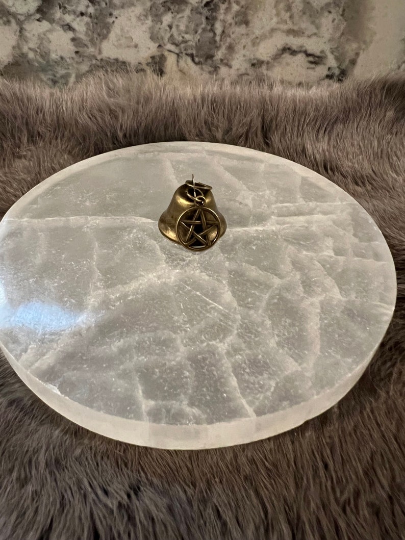 Pu&ograve; includere: Un piatto di ricarica in selenite bianco con una campana in ottone con un ciondolo a pentagramma.