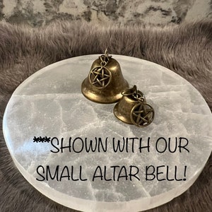 May include: Two gold-toned bells with a pentagram design on a white selenite altar plate. The text "***SHOWN WITH OUR SMALL ALTAR BELL!" is written on the plate.
