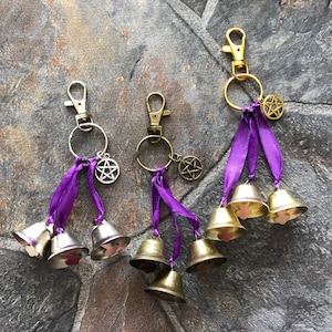 May include: Three silver keychains with purple ribbons and silver bells. Each keychain has a silver pentagram charm.