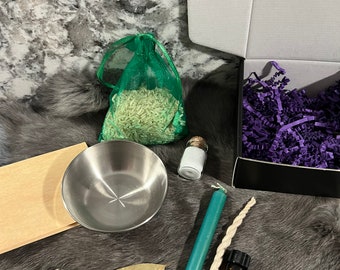 May include: A green mesh bag filled with uncooked rice, a small clear glass bottle with a white lid, a silver bowl, a green candle, a white twine, a brown bottle with a black lid, a small brown piece of wood, a green leaf, and a small grey stone.