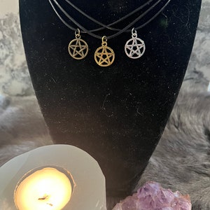 May include: Three silver, gold, and black pentagram necklaces on a black velvet display stand. The necklaces are on black cords.