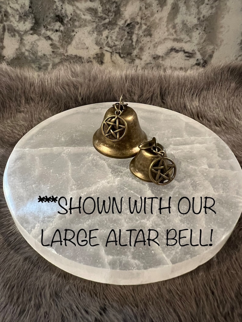 Pu&ograve; includere: Due campane dorate con un designo a pentagramma su una superficie rotonda bianca. Il testo "***SHOWN WITH OUR LARGE ALTAR BELL!" &egrave; scritto sulla superficie.
