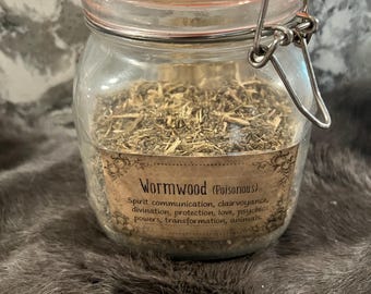 Könnte beinhalten: Ein Glasgefäß mit einem Metallverschlussdeckel, gefüllt mit getrockneten Kräutern, die mit "Wormwood (Poisonous)" beschriftet sind. Das Etikett listet die Verwendung des Krauts auf, darunter spirituelle Kommunikation, Hellsehen, Wahrsagerei, Schutz, Liebe, psychische Kräfte, Transformation und Tiere.