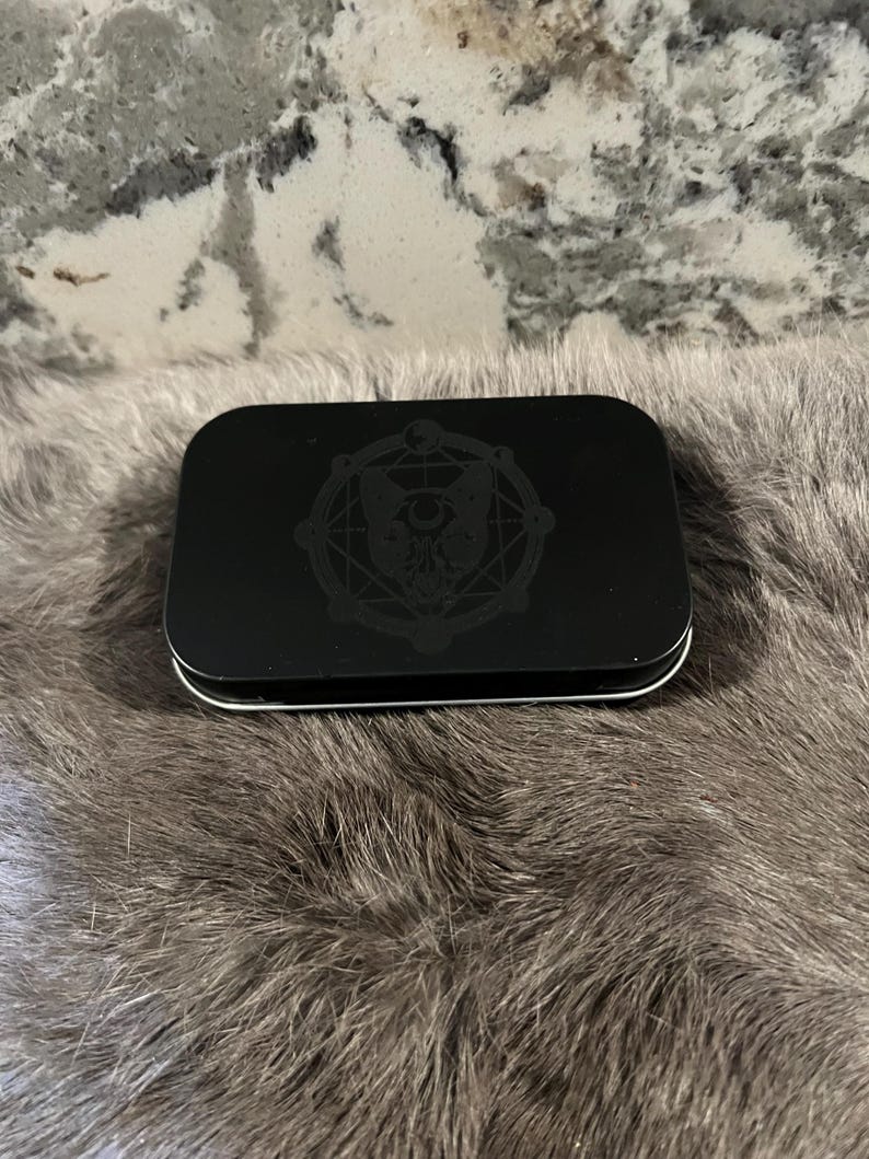 May include: A black metal tin with a circular design featuring a stylized owl with geometric patterns and the words "The Owl and the Pussycat".