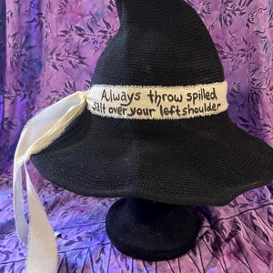 May include: Black witch hat with a white ribbon and the text "Always throw spilled salt over your left shoulder" written on the band.