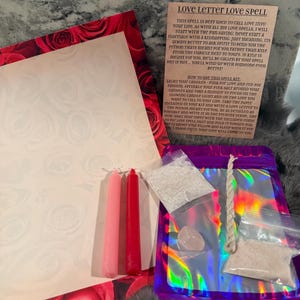 May include: A love spell kit featuring a sheet of paper with a red rose border, a pink candle, a red candle, a small clear bag of white powder, a small clear bag of pink powder, a polished rose quartz stone, a piece of twine, and an instruction card.