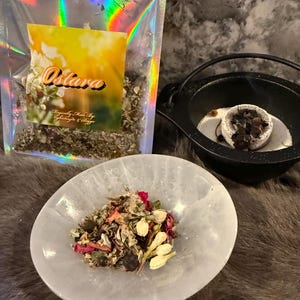 May include: A white bowl filled with a blend of dried herbs, flowers, and berries. The bowl is sitting on a brown fuzzy surface. A clear plastic bag with a label that says "Ostara" is in the background. The bag contains dried herbs and flowers.