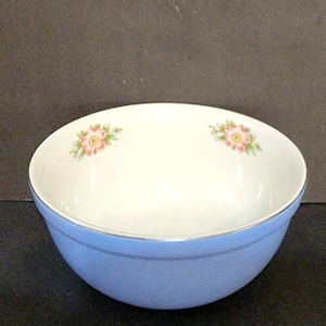 May include: A light blue mixing bowl with a white interior and a silver rim. The bowl has a floral design with pink roses on the rim.