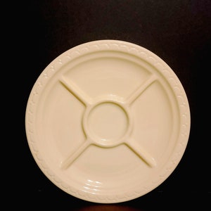 May include: A white ceramic serving dish with four sections and a central dip. The dish has a decorative scalloped edge.