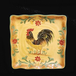 May include: A square ceramic serving dish with a yellow background and a hand-painted design of a rooster with red, black, and yellow accents. The rooster is surrounded by green leaves and red, yellow, and white flowers.