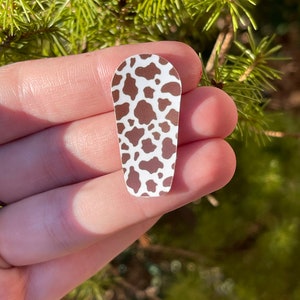 Puede incluir: Una pegatina de vaca marrón y blanca con forma rectangular redondeada.