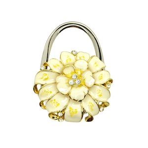 May include: A white and yellow flower-shaped handbag hook with rhinestones. The hook is made of metal and has a silver finish.