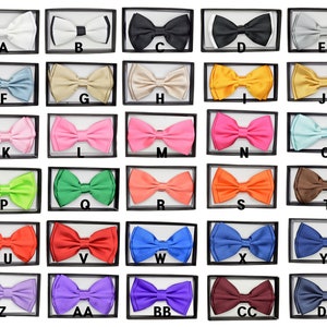 May include: A collection of 26 bow ties in various colors and patterns, displayed in individual boxes. The boxes are arranged in four rows of six boxes each. The bow ties are made of satin and have a variety of colors, including black, white, red, blue, green, yellow, orange, pink, purple, and brown.