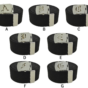 May include: Seven black canvas belts with silver buckles featuring a different letter of the alphabet in a gothic font on each buckle. The letters are A, B, C, D, E, F, and G.