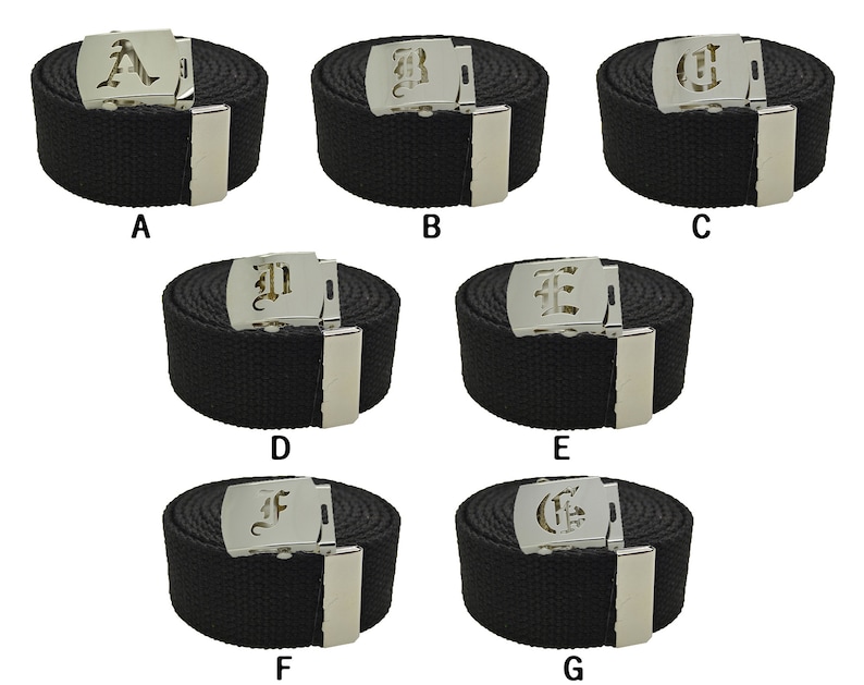May include: Seven black canvas belts with silver buckles featuring a different letter of the alphabet in a gothic font on each buckle. The letters are A, B, C, D, E, F, and G.