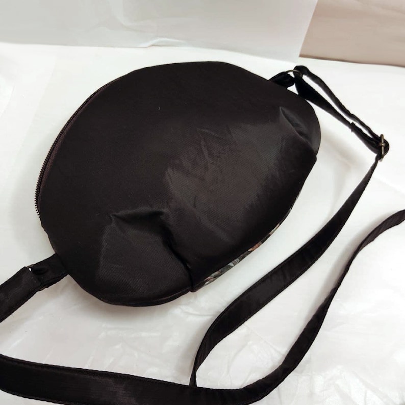 May include: A black crossbody bag with a zipper closure and a long adjustable strap. The bag is made of a smooth, water-resistant fabric.