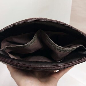 May include: A brown leather crossbody bag with a zipper closure and two interior pockets. The bag is open and the interior is visible.