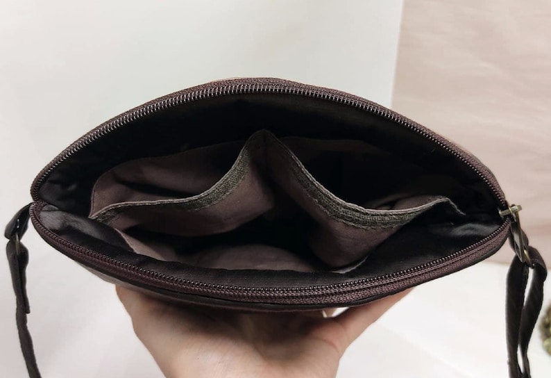 May include: A brown leather crossbody bag with a zipper closure and two interior pockets. The bag is open and the interior is visible.