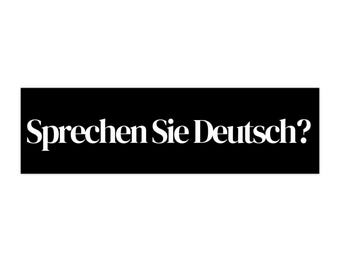 May include: A black rectangular sign with the white text "Sprechen Sie Deutsch?" The text is in a serif font. The background is plain white.