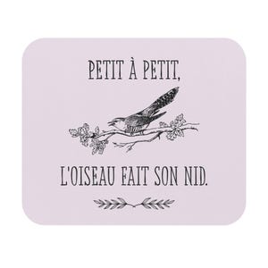 May include: A light purple square coaster with a black illustration of a bird perched on a branch. The text "PETIT À PETIT, L'OISEAU FAIT SON NID" is printed in black above and below the bird illustration.