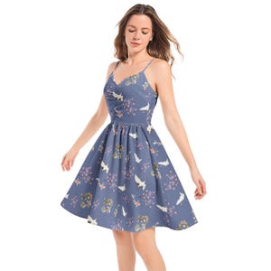 May include: A knee-length blue dress with thin spaghetti straps and a ruched bodice. The fabric features a repeating pattern of white cranes, orange koi fish, and small purple floral clusters scattered across the entire surface of the garment.