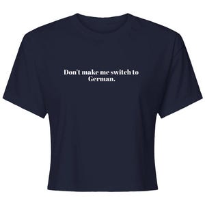 May include: A dark navy blue short-sleeved crop top featuring the white text "Don't make me switch to German." printed in a clean, centered serif font across the chest area. The garment has a crew neckline and a straight hemline.