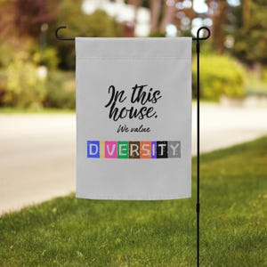 May include: A white garden flag with black text that reads "In this house, we value DIVERSITY". The word "DIVERSITY" is spelled out in colorful blocks.