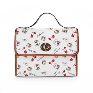 Könnte beinhalten: Weiße Handtasche mit braunem Besatz und Griff. Die Tasche hat ein Muster aus roten Rollern, Kaffeetassen und italienischen Sätzen. Sie hat einen goldenen Verschluss und einen braunen Ledergriff.