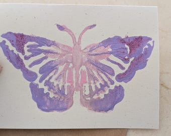 May include: A purple and pink butterfly with a white outline is painted on a light beige card.