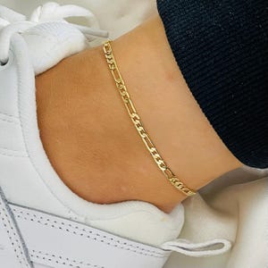 May include: A gold chain ankle bracelet with a curb link design.