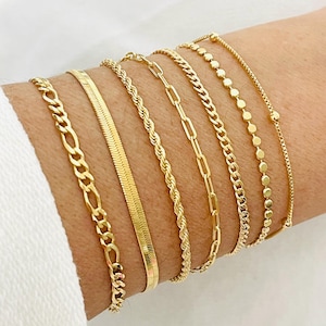 May include: A set of seven gold chain bracelets, featuring different chain styles, including a curb chain, a rope chain, a box chain, and a beaded chain.