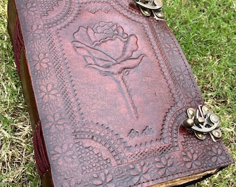 May include: A brown leather journal with a rose design embossed on the cover. The journal has two brass clasps to keep it closed.