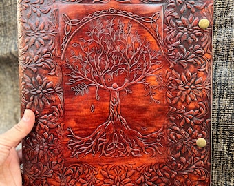 Può includere: Un diario in pelle marrone con un design a rilievo di un albero della vita con radici e rami intricati. La copertina è decorata con motivi floreali e ha due accenti in ottone.