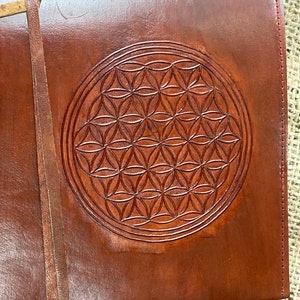 Könnte beinhalten: Ein braunes Lederjournal mit einem geprägten Design der Blume des Lebens auf dem Einband.