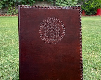 May include: A brown leather journal with a stitched border and a flower of life design embossed on the front cover.