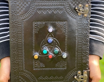 Può includere: Un diario in pelle nera con un designo in rilievo intricato e un motivo a nodo celtico. Il diario ha una chiusura a fibbia ed è adornato con pietre preziose colorate.