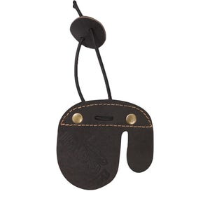 May include: A black leather archery finger tab with a brown stitching detail and two brass rivets. The tab has a strap with a black loop for attaching to the wrist.