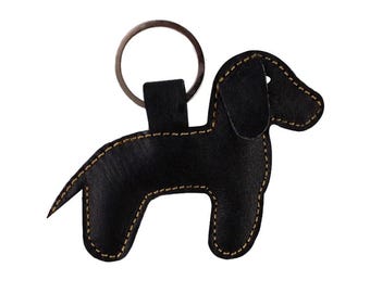 May include: Black leather dog keychain with a gold stitched outline. The keychain has a silver metal ring.
