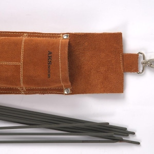 Leather Welding Rod Pouch | Handmade Welder Rod Holder, A brown leather welding rod holder with the text "AKSNOOR" and a silver clasp. Several dark gray welding rods are visible, lying next to the open holder. The holder is made of a soft, textured leather.