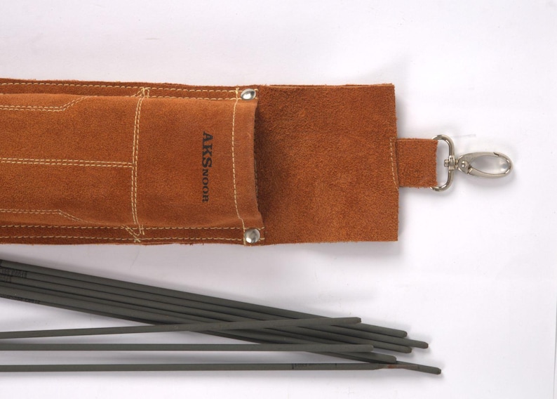 Leather Welding Rod Pouch | Handmade Welder Rod Holder, A brown leather welding rod holder with the text "AKSNOOR" and a silver clasp. Several dark gray welding rods are visible, lying next to the open holder. The holder is made of a soft, textured leather.