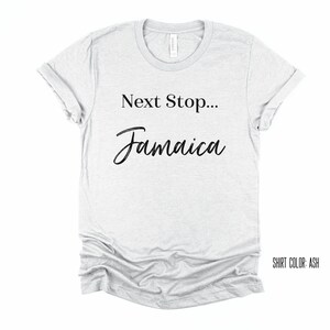 May include: A light grey t-shirt with the text "Next Stop... Jamaica" in black lettering. The shirt colour is ash.
