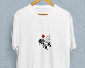 May include: White t-shirt with a black and white illustration of a bee flying with a red circle above it.